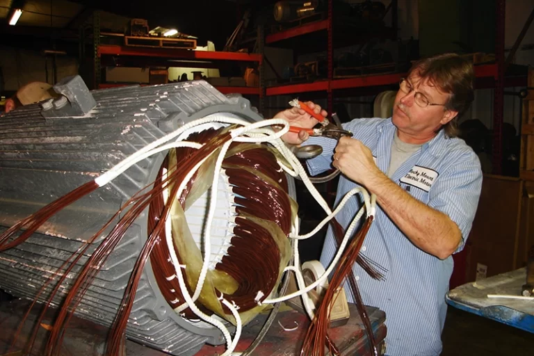 A middle aged mechanic connects cables together while performing electric motor rewinding.