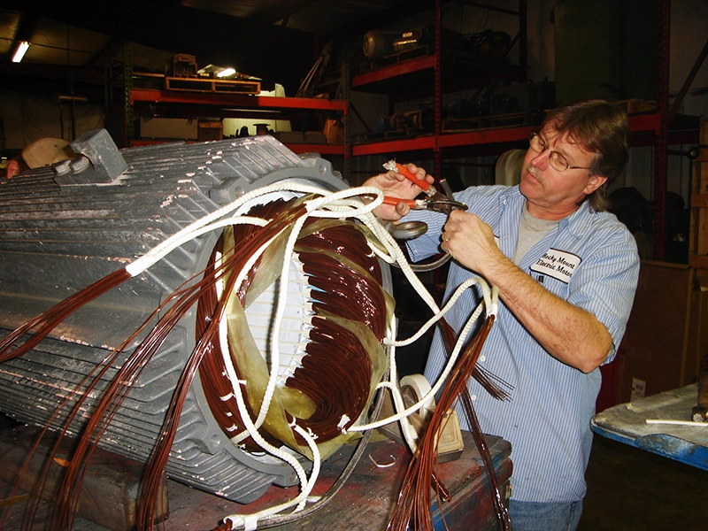 A middle aged mechanic connects cables together while performing electric motor rewinding.