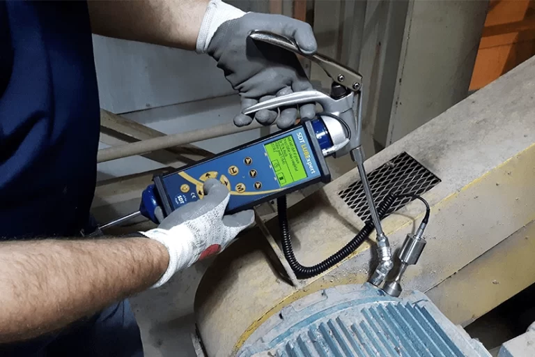 A man performs predictive maintenance by using a lubrication tool to ensure electric motor lubrication is done correctly.