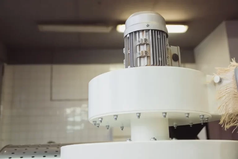 An industrial electric motor sits upright atop a large, white metal industrial installation.